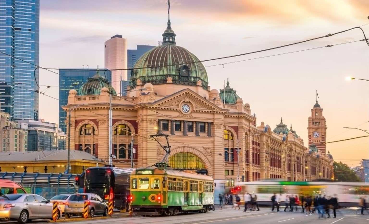 Trams and pedestrians crossing the intersection in front of Flinders St Station at dusk.