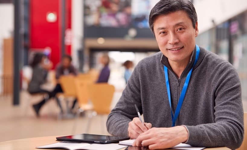 Portrait of male adult student with digital tablet working at a table a university hall.