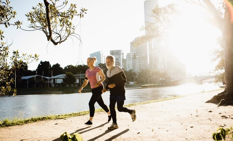 Two people running along the Yarra River on a bright day.